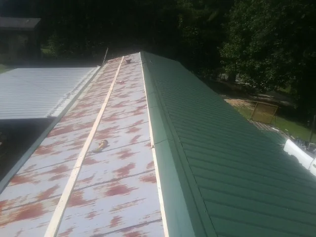 Old rusted panels beside newly installed green metal roofing — Wind Damage Roof Repair by Roofing Brothers in Dorothy