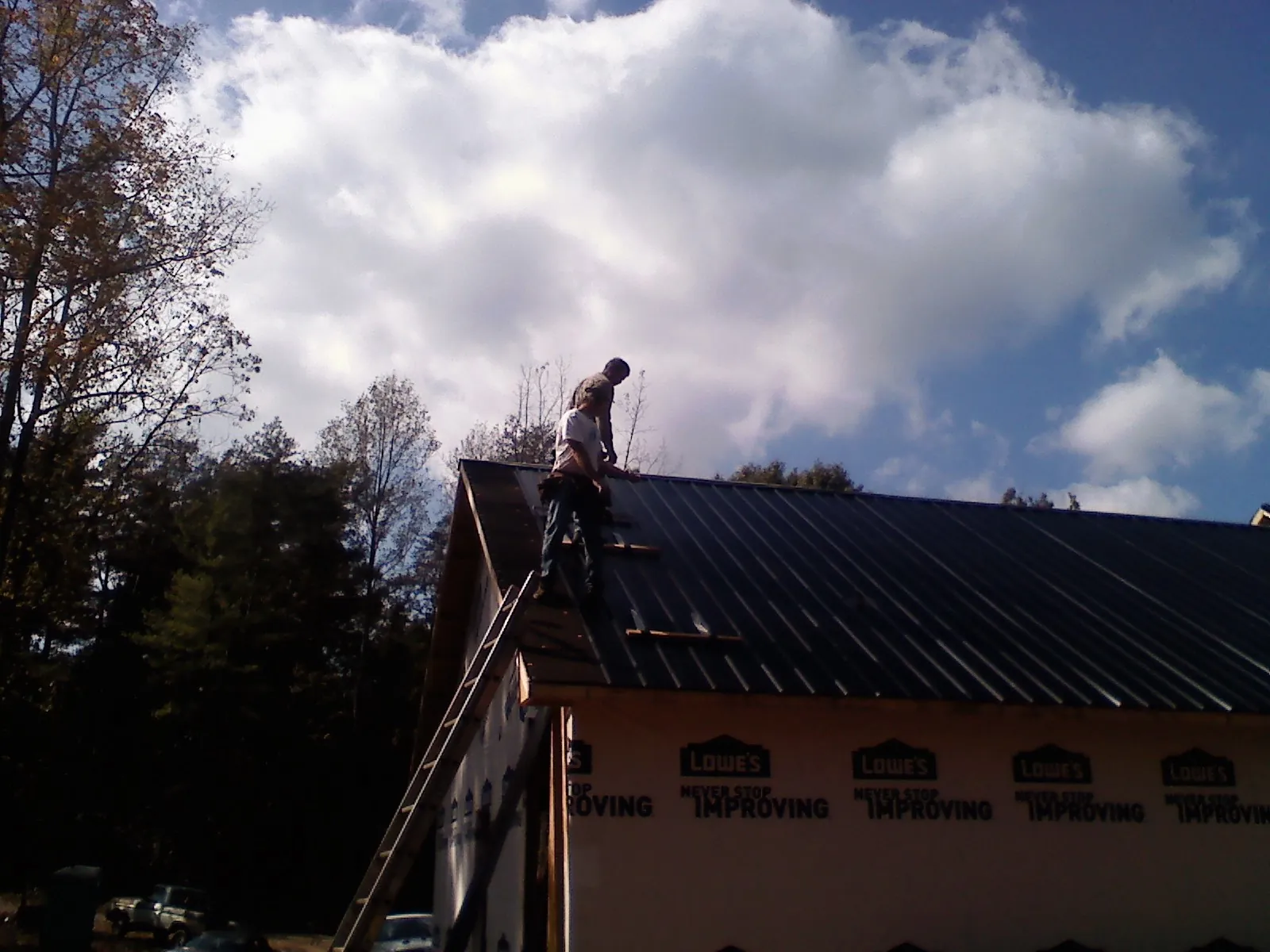 Roofer fastening dark metal panels high against a cloudy sky, from a Roof Inspection job in Dorothy