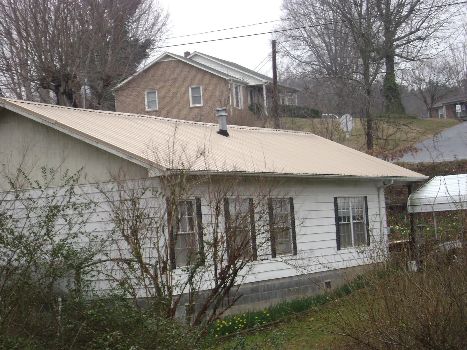 Tan metal roof on a white sided house set into a hillside — Commercial Roofing by Roofing Brothers in Dorothy