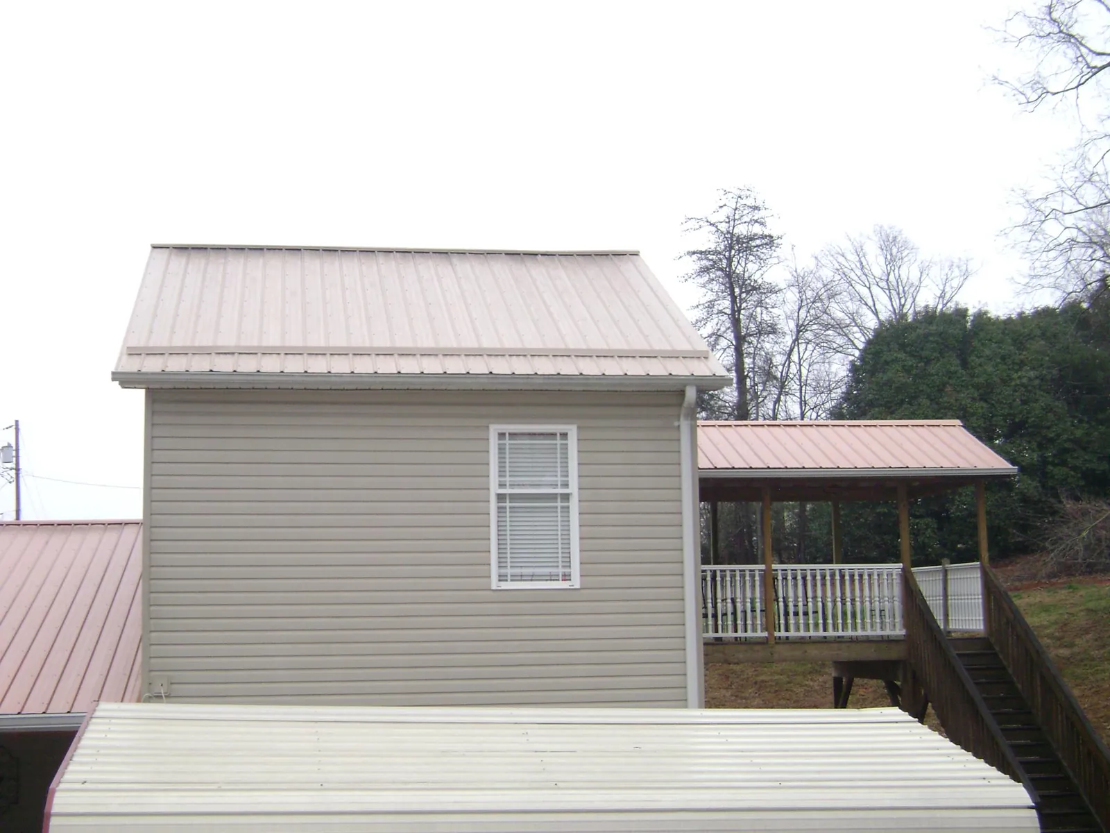 Tan metal roofs on a two story addition and attached porch, from a Roof Replacement job in Dorothy